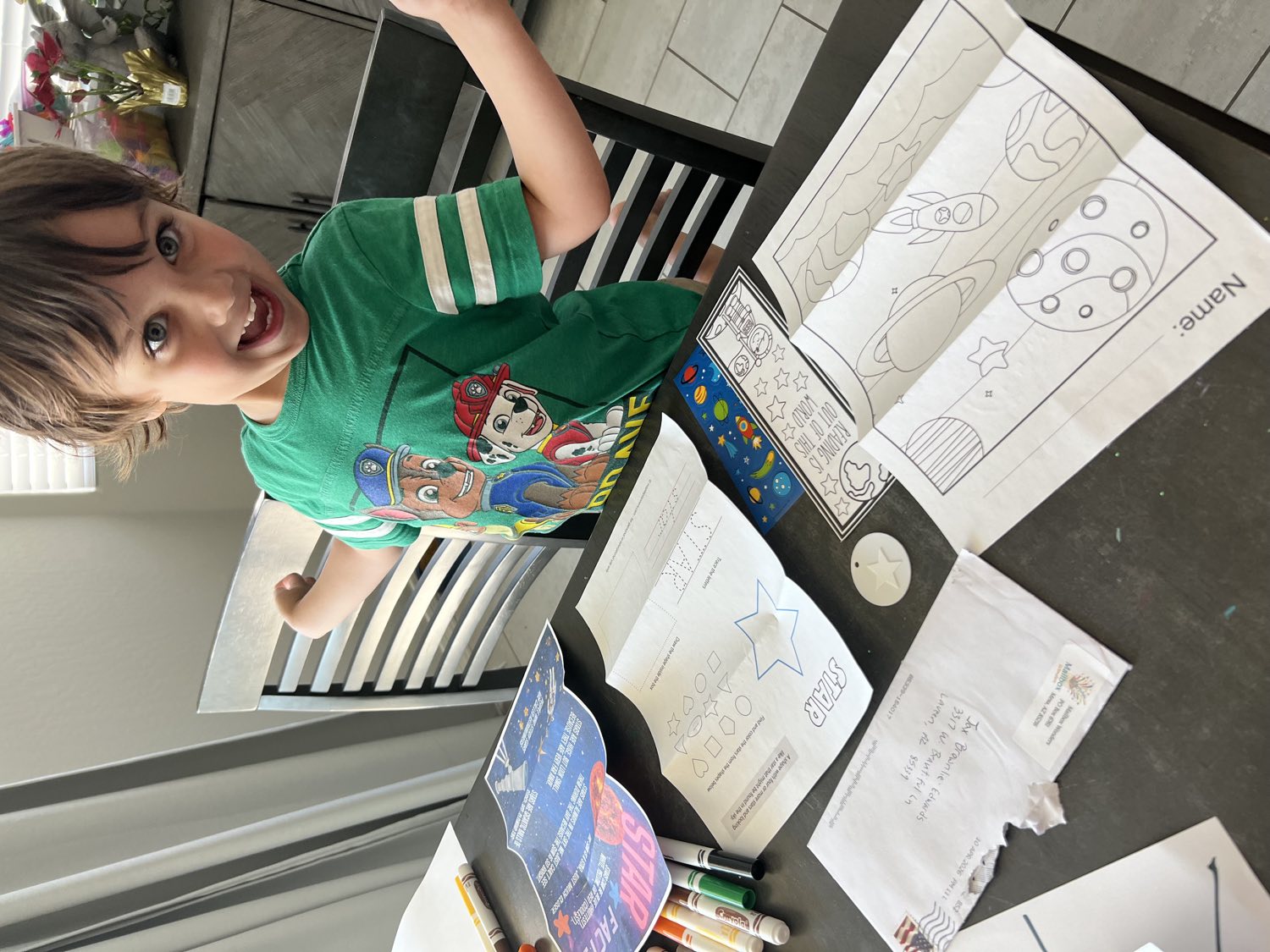 A boy grinning next to his space-themed Mailbox Wonders coloring pages